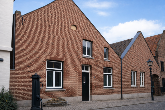 Roodbakstenen huis met witte kozijnen en een blauwe lucht op de achtergrond.